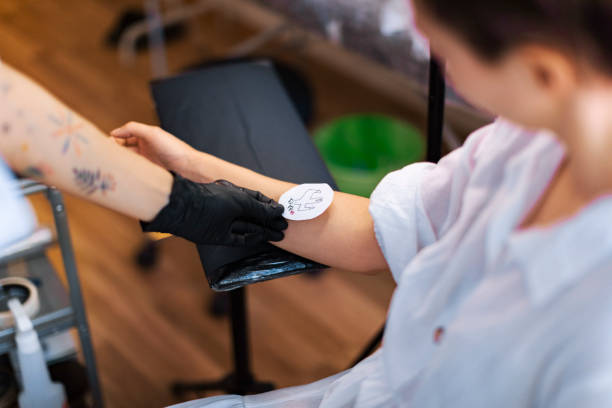 Artist applies stencil to arm; tattoo ink used.