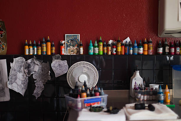 Tattoo studio shelf lined with colorful tattoo ink bottles and stencils against red wall.