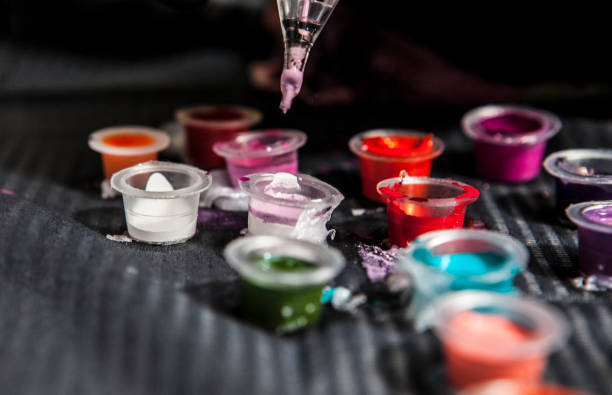 Dropper dispensing purple tattoo ink into small caps on black surface.