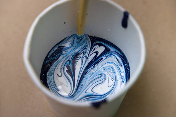 Blue and white tattoo ink swirled in cup, mixed with wooden stick.
