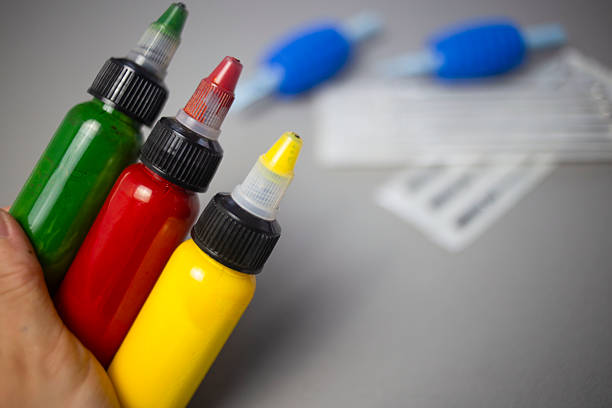 Hand holds three squeeze bottles of green, red, and yellow tattoo ink.
