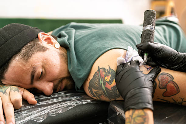 Tattoo artist works on client’s arm with black-gloved hand and tattoo ink.

