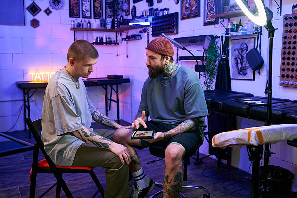 Two artists discuss design on tablet in tattoo shop
