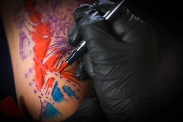 Artist applies vibrant red and blue tattoo ink to outlined design on skin.
