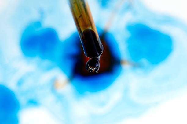 Dropper releasing a drop of dark tattoo ink into swirling blue liquid.