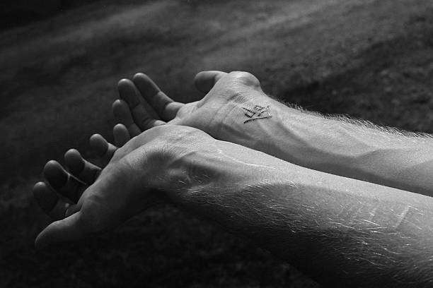 Black and white hands showing a minimalist symbol applied with fine tattoo ink.