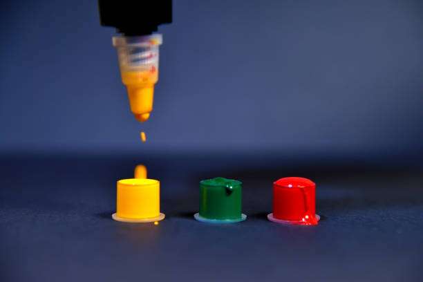 Tattoo machine drips vibrant yellow tattoo ink into a cap, alongside green and red.