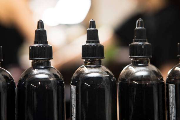 Row of black bottles with dropper caps, containing professional tattoo ink.