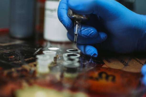 Artist dips tattoo machine into black tattoo ink, ready for a new design.