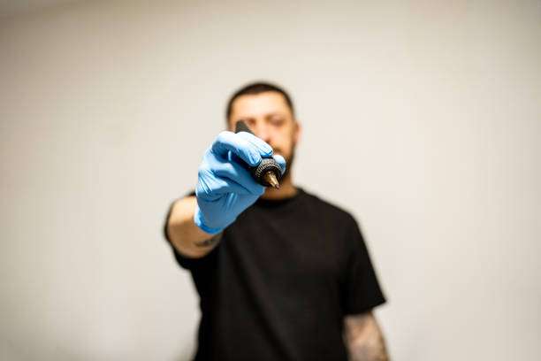 Hand in blue glove holding tattoo machine needle, tattoo ink.