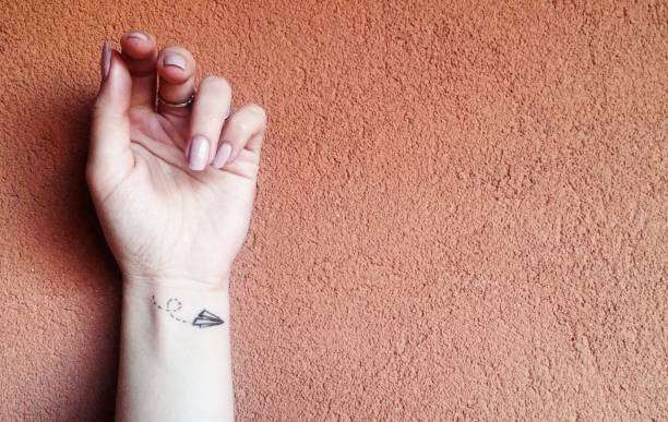 Small paper airplane tattoo on a wrist, featuring crisp black tattoo ink design.